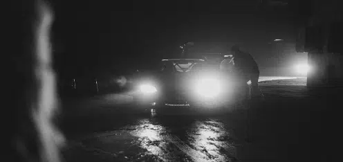 Carro con luces encendidas en la oscuridad. Imagen a blanco y negro