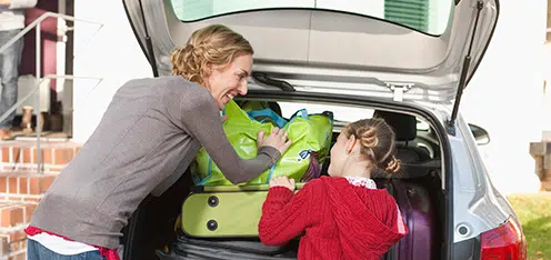 Mamá e hija, organizando maletas de viaje en el baúl de carro