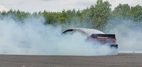 Carro negro generando humo blanco en una pista